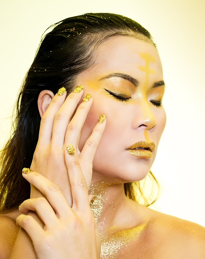 Beauty-Porträt mit Gold-Make-up und Glitzer, geschlossene Augen, heller Studiogrund